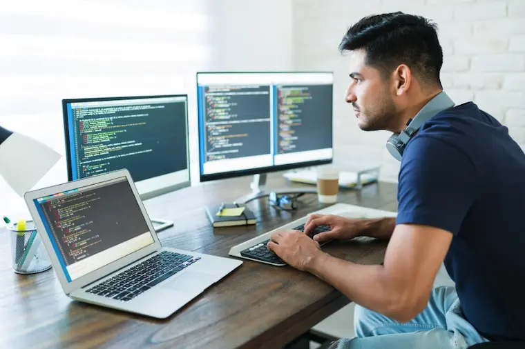 Stockfoto: Programmierer arbeitet an mehreren Bildschirmen mit Code – moderner Arbeitsplatz in der Softwareentwicklung und IT.
